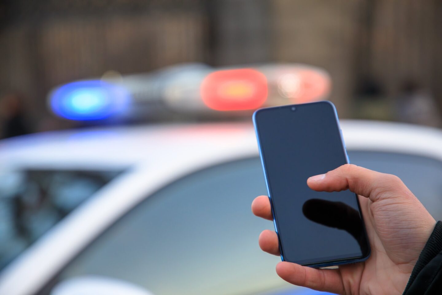Zoomed in on a hand holding a cellphone in front of a police car
