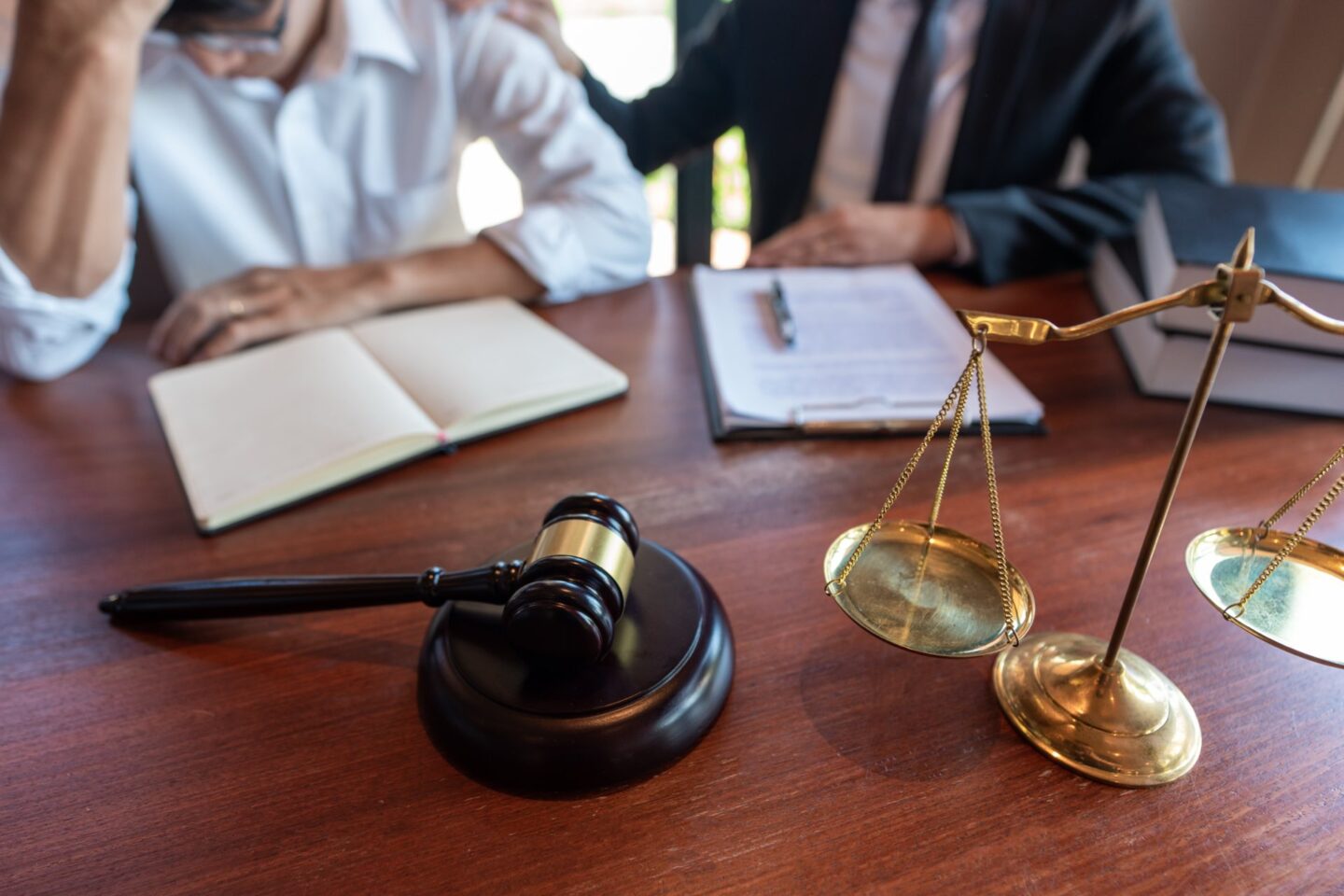 Zoomed in picture of two people sitting at a desk one person with their head in their hand next to a gavel and notebooks